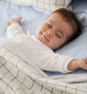 Smiling baby girl lying on a bed sleeping on blue sheets